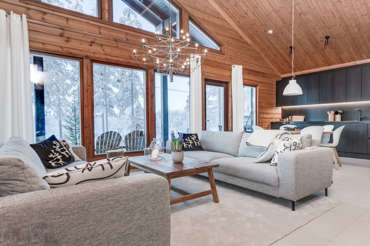 Open living room with high timber ceiling, grey sofas and tall windows onto the snowy forest