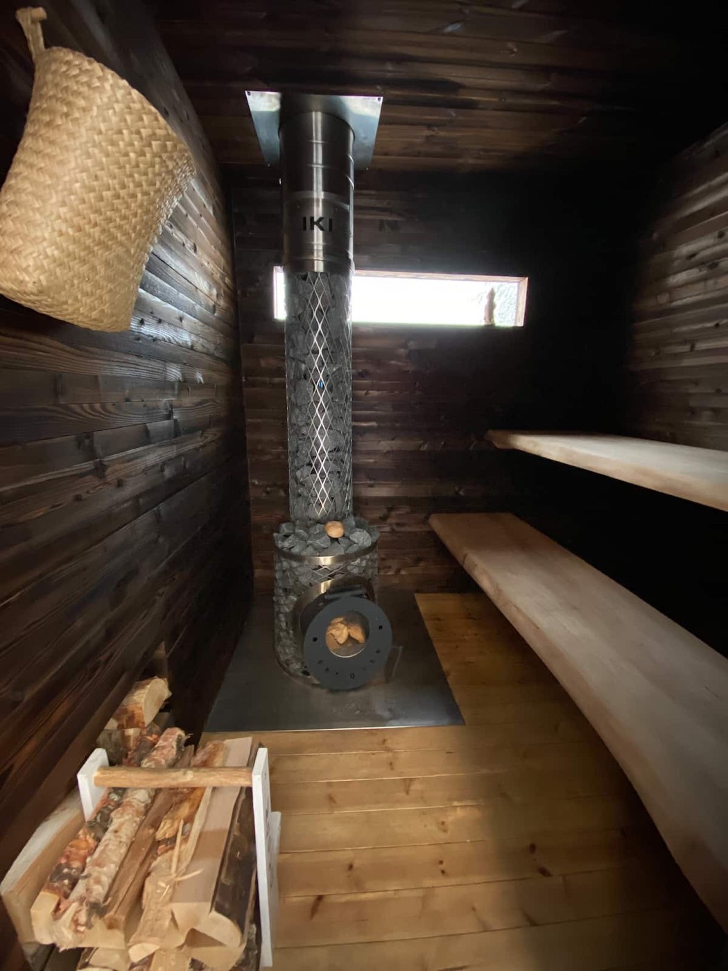 Inside the wood-burning sauna, dark timber benches and a tall wood stove